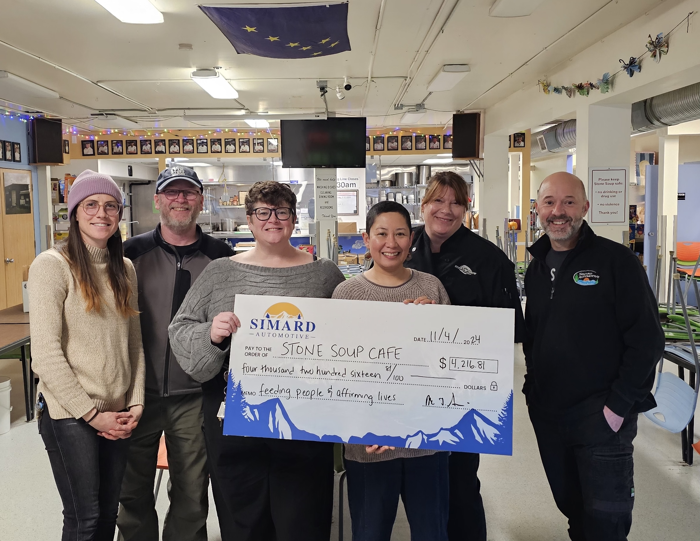 Group picture of the Bread Line Staff & Mike Simard, of Simard Automotive, holding a novelty donation check at the Bread Line's soup kitchen.